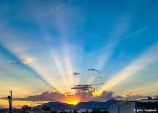 Sunbeams over the Hills – Crepuscular rays fanning from a setting sun over distant hills.