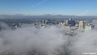 Sea of Fog over Downtown Sacramento – Morning fog rolls over Sacramento like an ocean, with only the tallest downtown towers breaking through under a clear blue sky. Aerial photograph © John England.