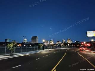 Road into the Sacramento Skyline – Road leading toward the lit Sacramento skyline at blue hour, West Sacramento, CA. Apr 2021. John England.