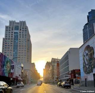 Sunrise Down a Downtown Street – Sunrise light down a downtown Sacramento street lined with towers and a mural, CA. Feb 2023. John England.